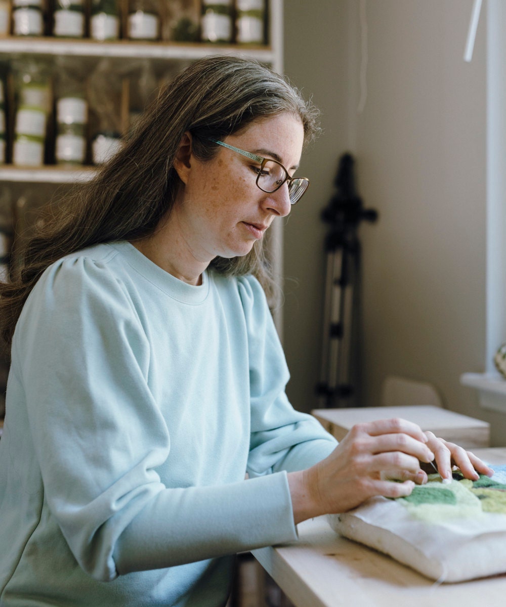 Elizabeth pokes her felting needle into a work-in-progress of her Grazing Sheep landscape