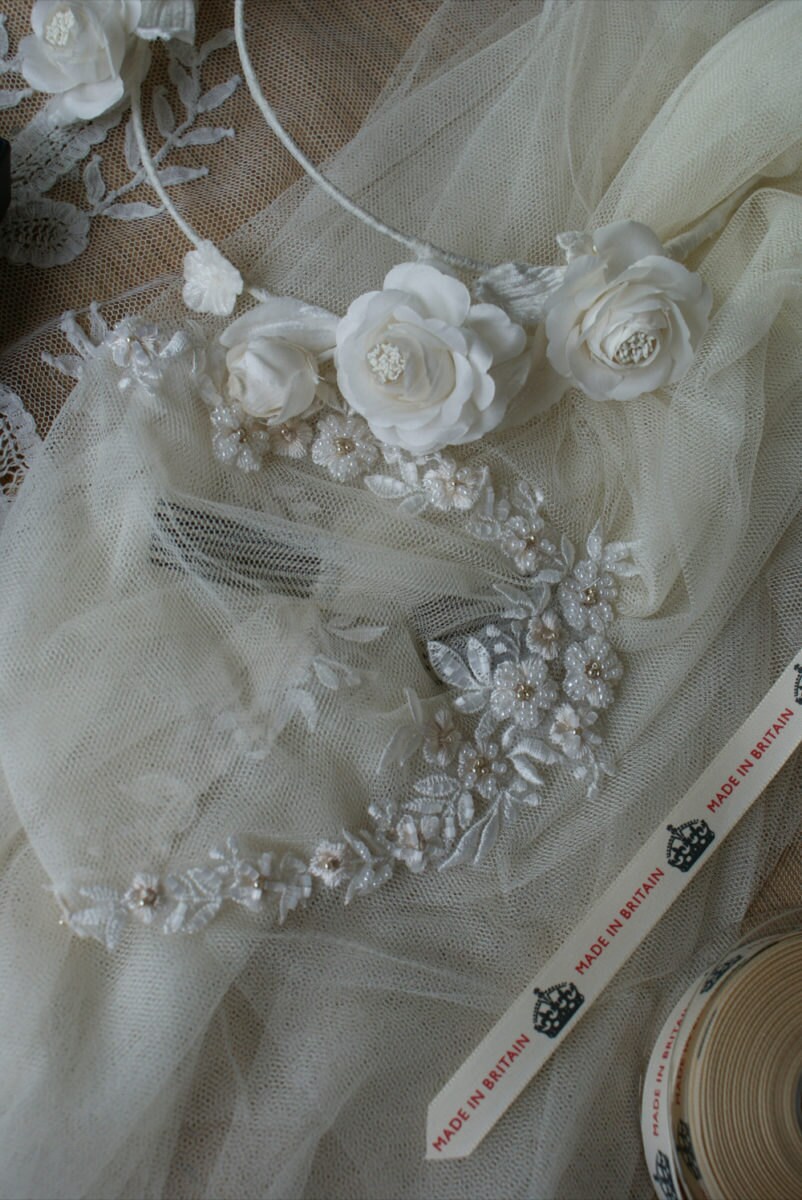 Details on a veil with a floral trim, loosely piled on Rae's workbench.