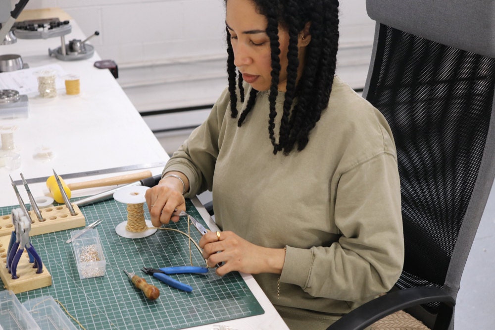 Sabrina at her work bench assembling a gold necklace.