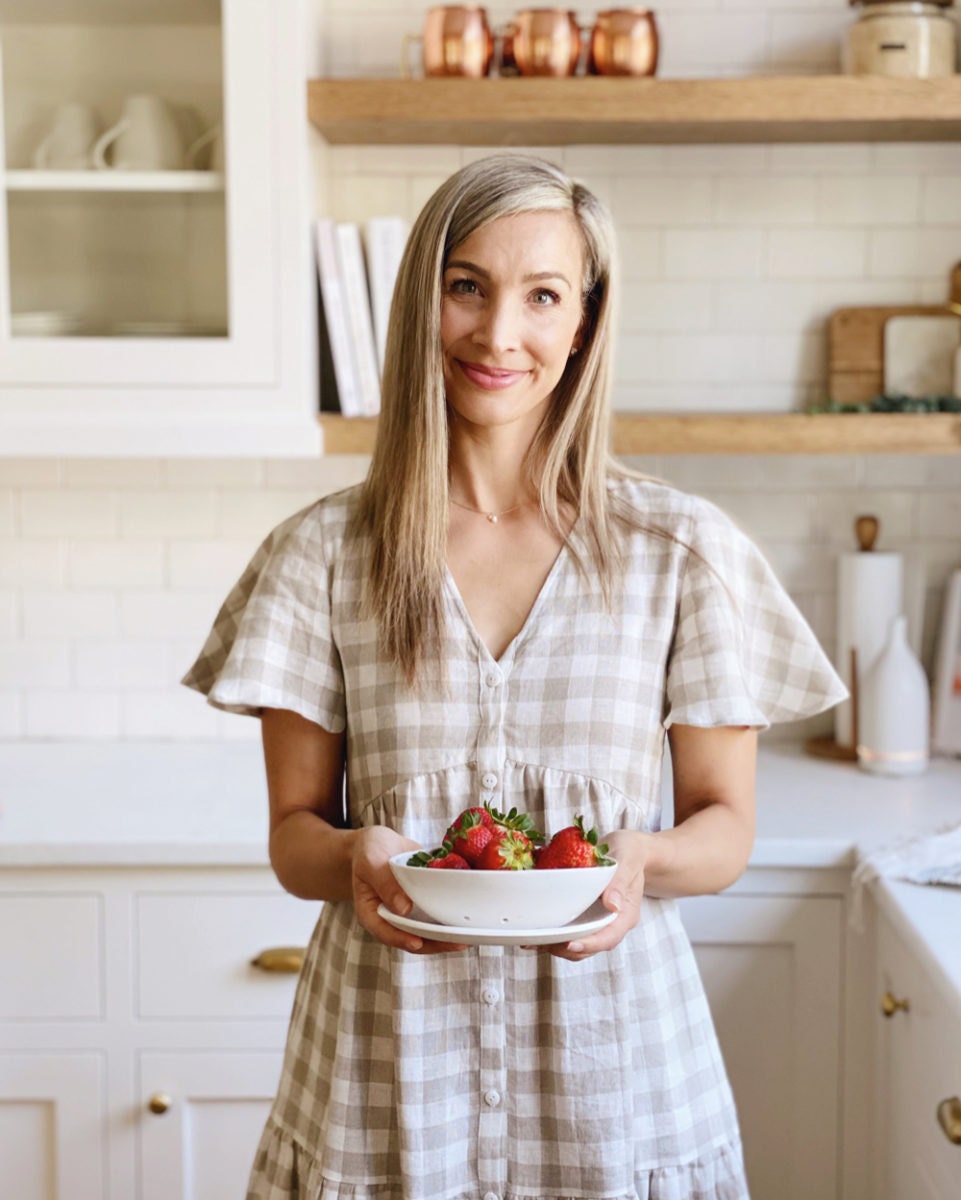 Kristine poses in the kitchen holding a berry bowl from Etsy and wearing a checkered linen dress from Etsy.