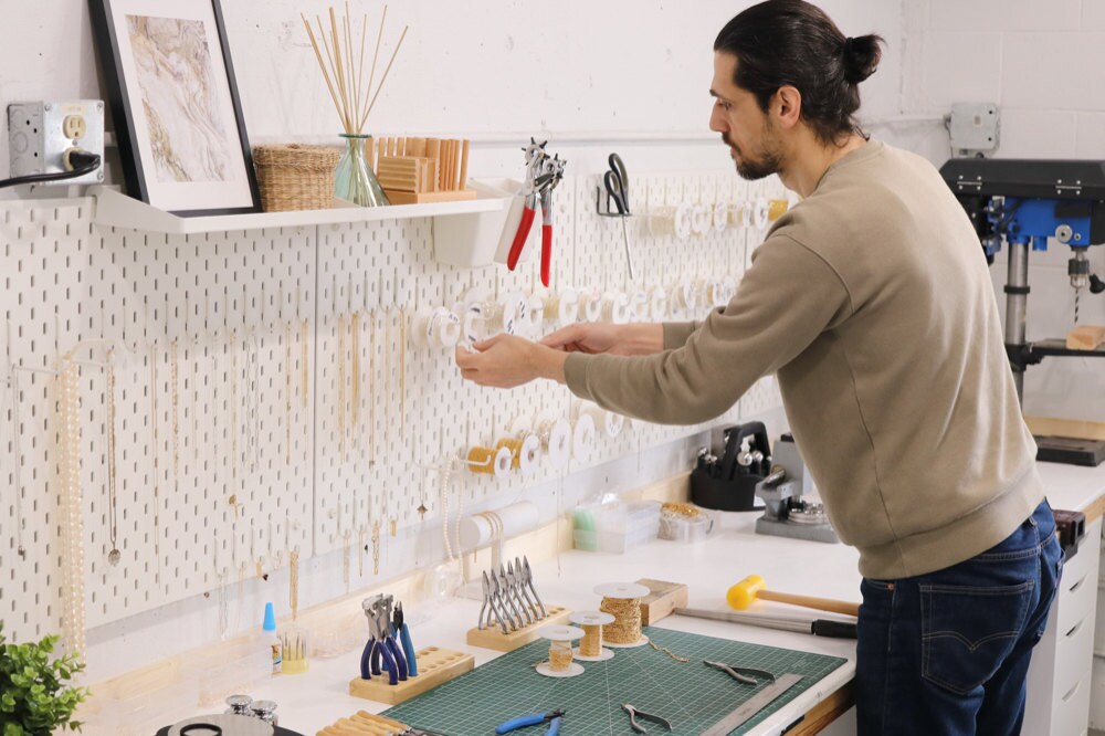 Sabrina's partner, Abe, organizing various spools of gold and silver chains above the studio workbench.