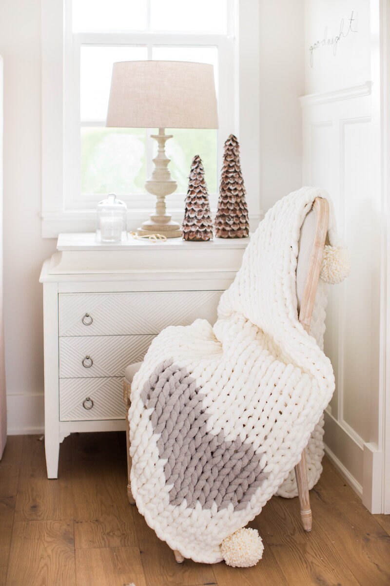 White chunky knit blanket draped over a chair in front of a bedroom window