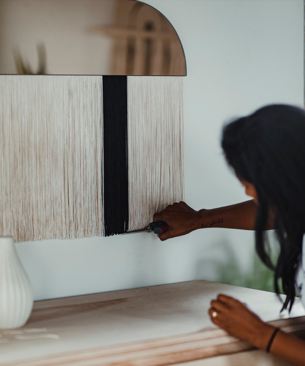 Candice trims threads on a fringed mirror piece.