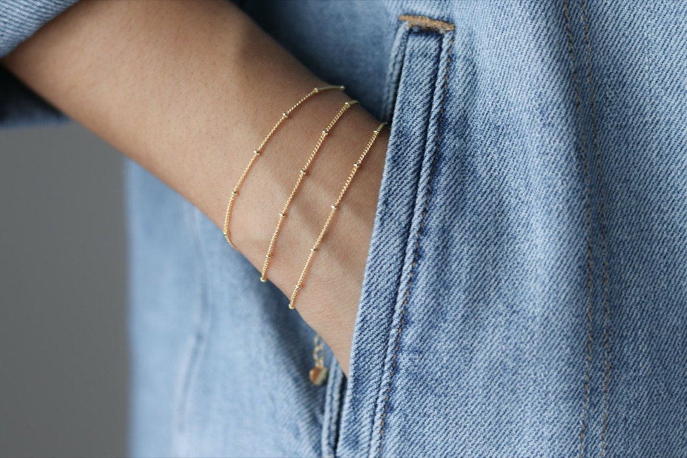 A woman wears a stack of 3 dainty beaded gold bracelets.