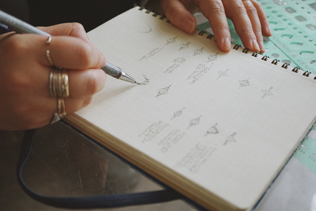 Katherine sketches ring designs in a notebook