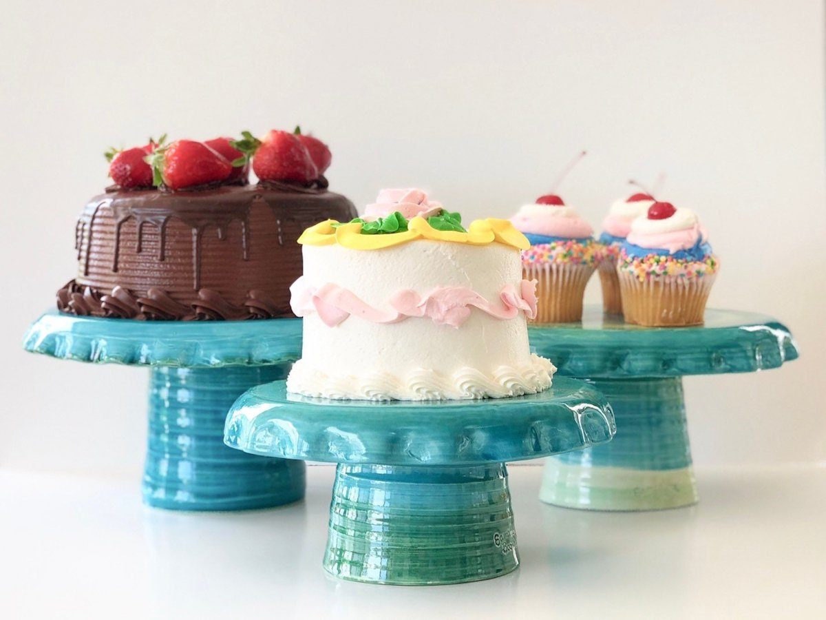 A trio of turquoise ceramic cake stands displaying fancy cakes.