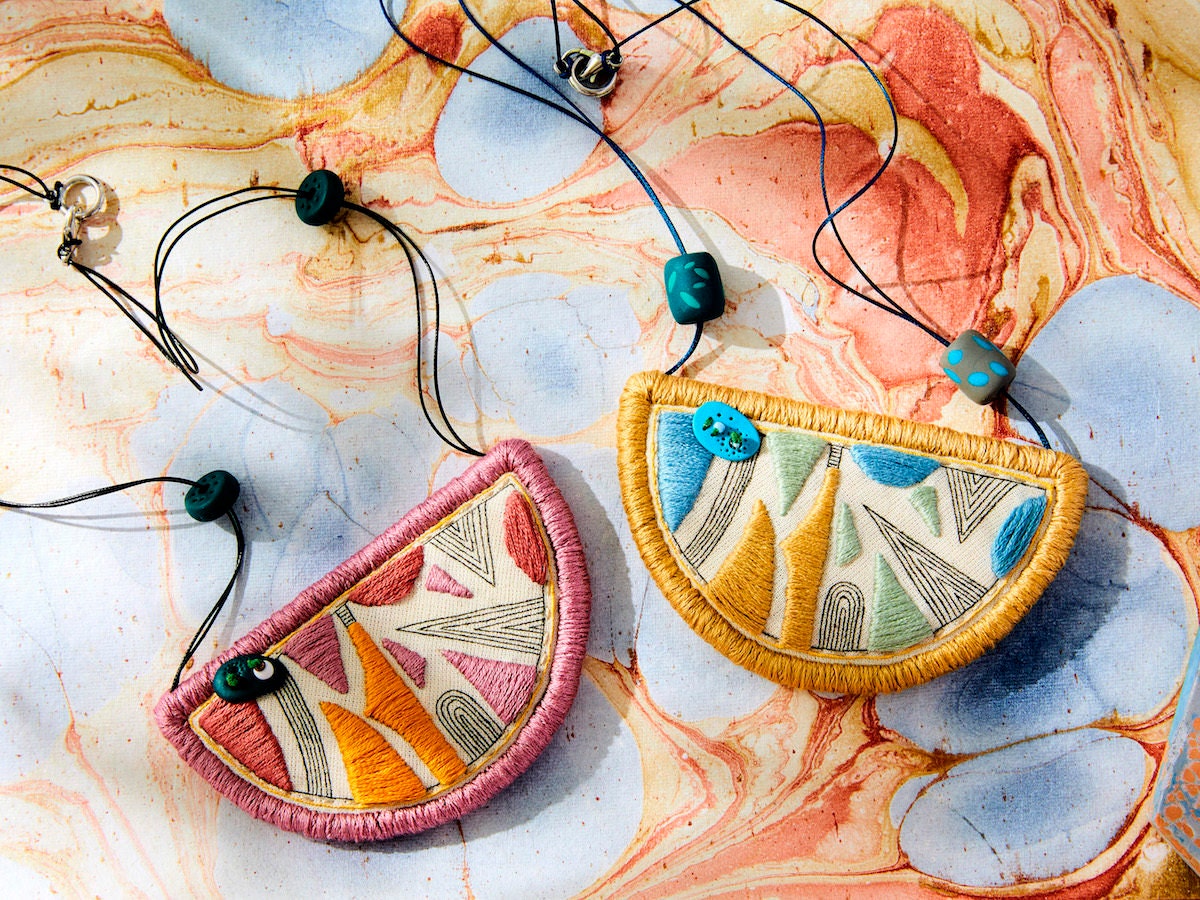 Two geometric embroidered bib necklaces from Perrrce styled on a colorful marbled paper backdrop