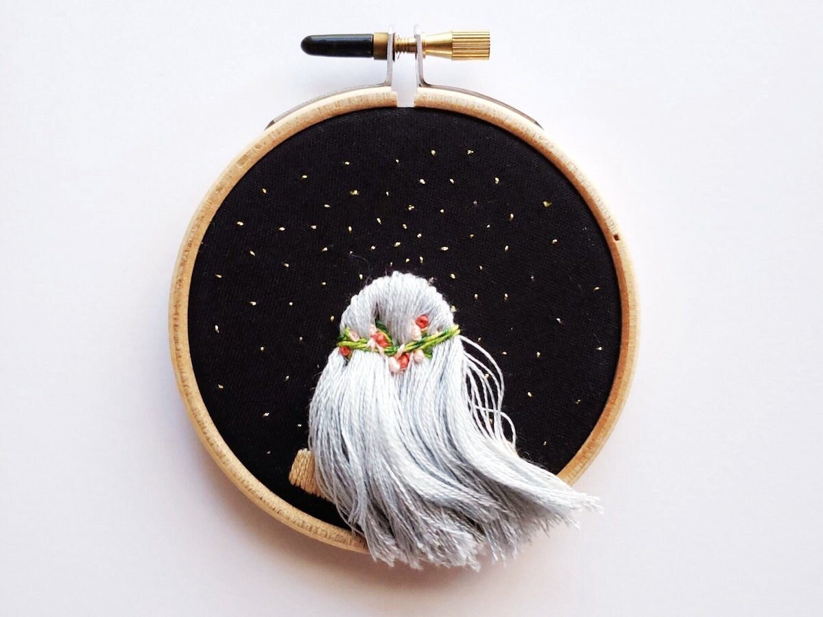 Embroidery hoop art from Desert Eclipse Studio featuring the back of a girl's head as she looks at the stars.