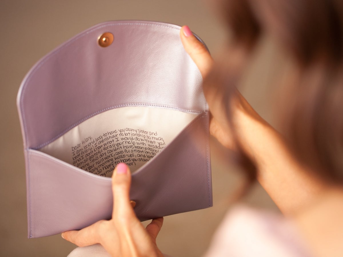 A woman holds open a personalized clutch from Fontém, reading the note inside.