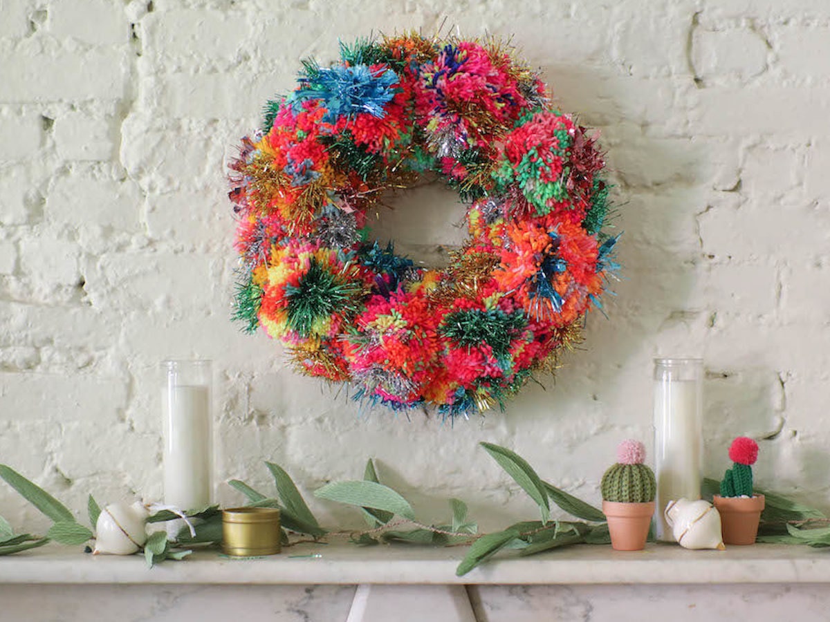 Rainbow pom-pom and tinsel wreath hangs above a mantel