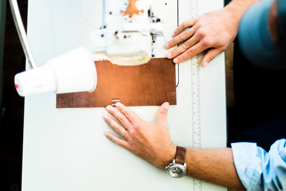 A Holtz Leather Co. employee works on stitching a leather wallet together.