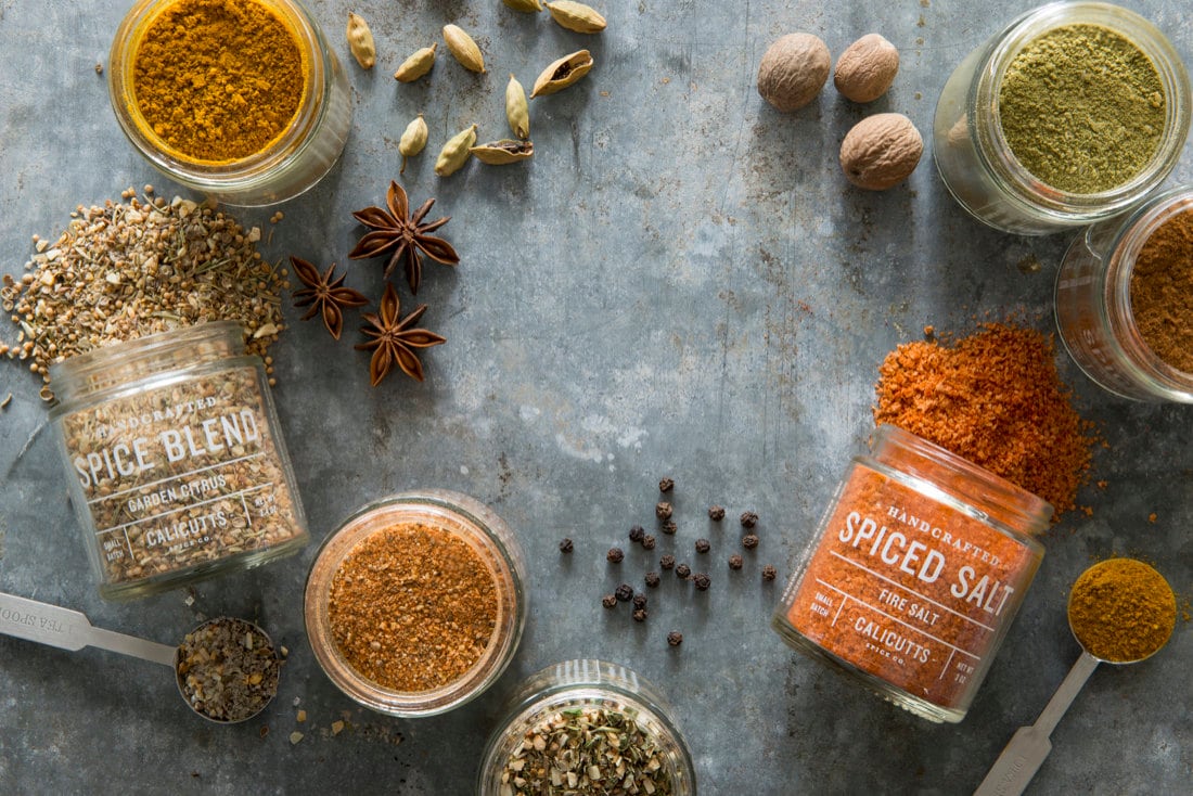 Jars of Calicutts Spice Co. blends pictured alongside the whole seeds that are used to make them.