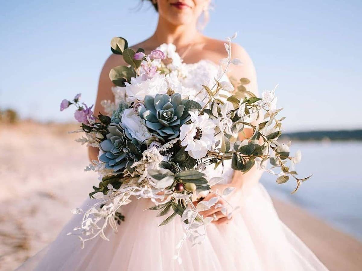 A real Faux Bouquets bride holds a succulent bouquet on the beach