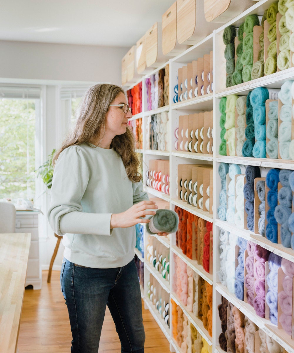 Elizabeth selects some roving from a wall of colored felts.