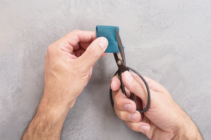 Steel shears trim leather along an angled line from one bottom corner of the strip to the pen mark at the top