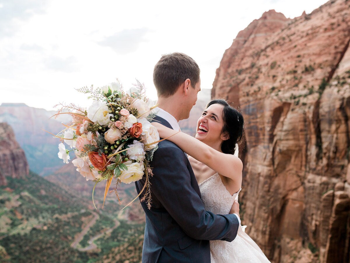 A real Faux Bouquets bride and groom embracing on the edge of a canyon, with her desert-hued bouquet in full display