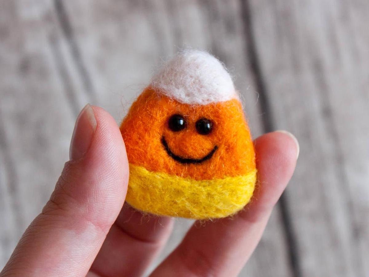 A needle felted candy corn brooch with a smiling face from znmystery.