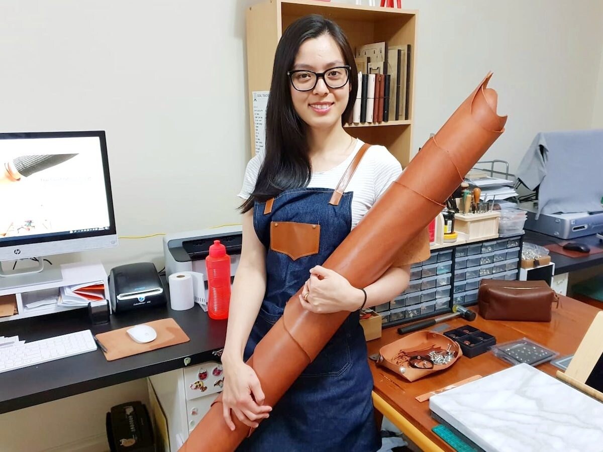 Pauline stands in her home studio holding a scroll of leather