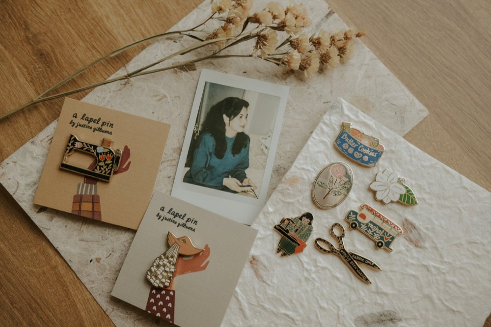 A photograph of Justine's mother pictured alongside a batch of enamel pins inspired by her.