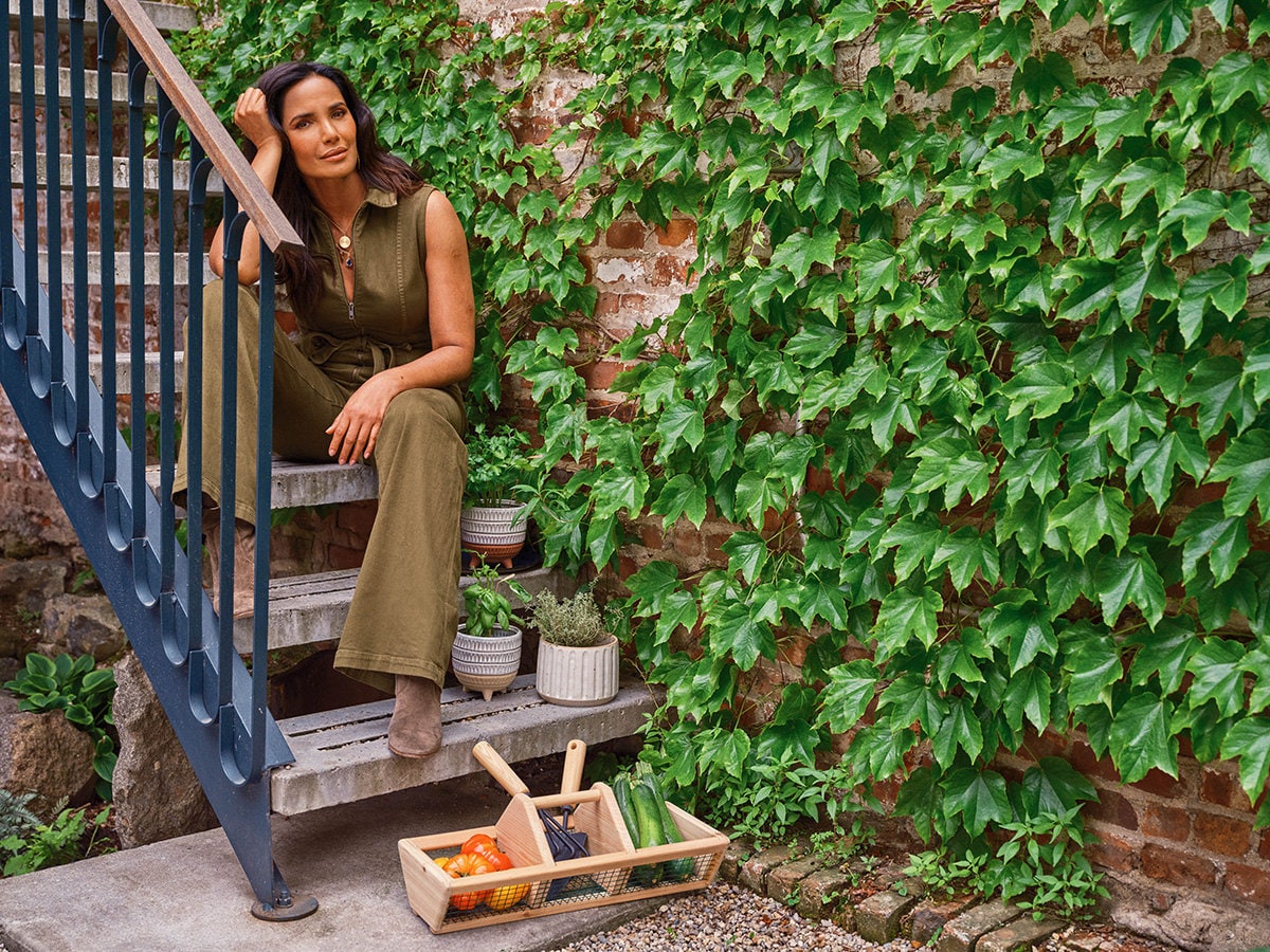 Padma Lakshmi sits on a staircase surrounded by gardening tools and herbs