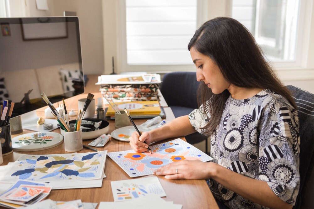 Meenal works on an illustrated print at her desk, adding detail with a pencil