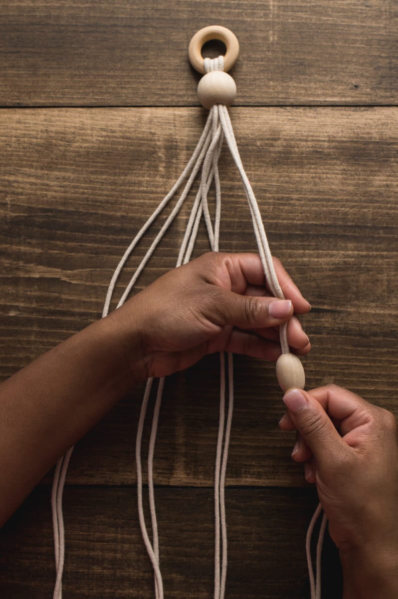 Hands separate the eight ropes into four groups of two and add a bead to each.