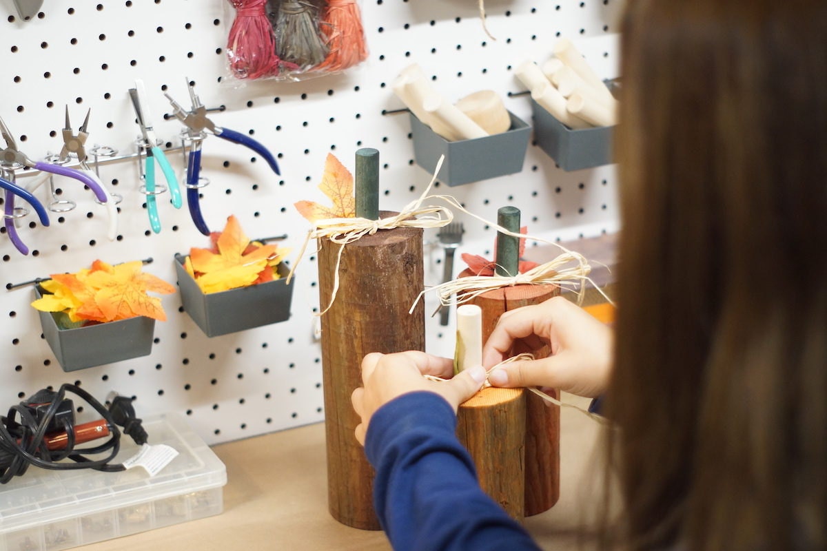 Sarah ties a piece of rafia onto a wooden pumpkin