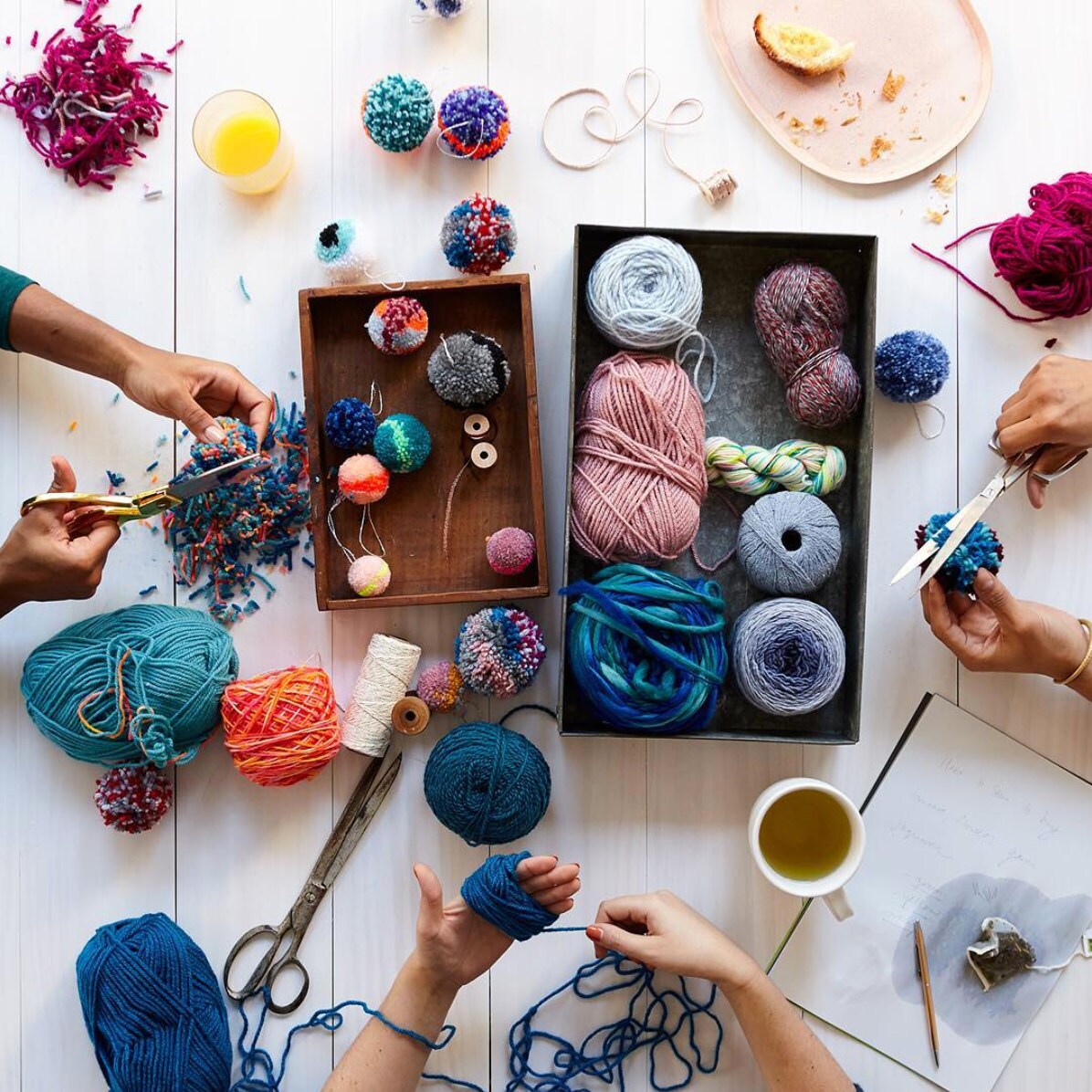 Hands at work making pom-poms while surrounded by colorful craft supplies