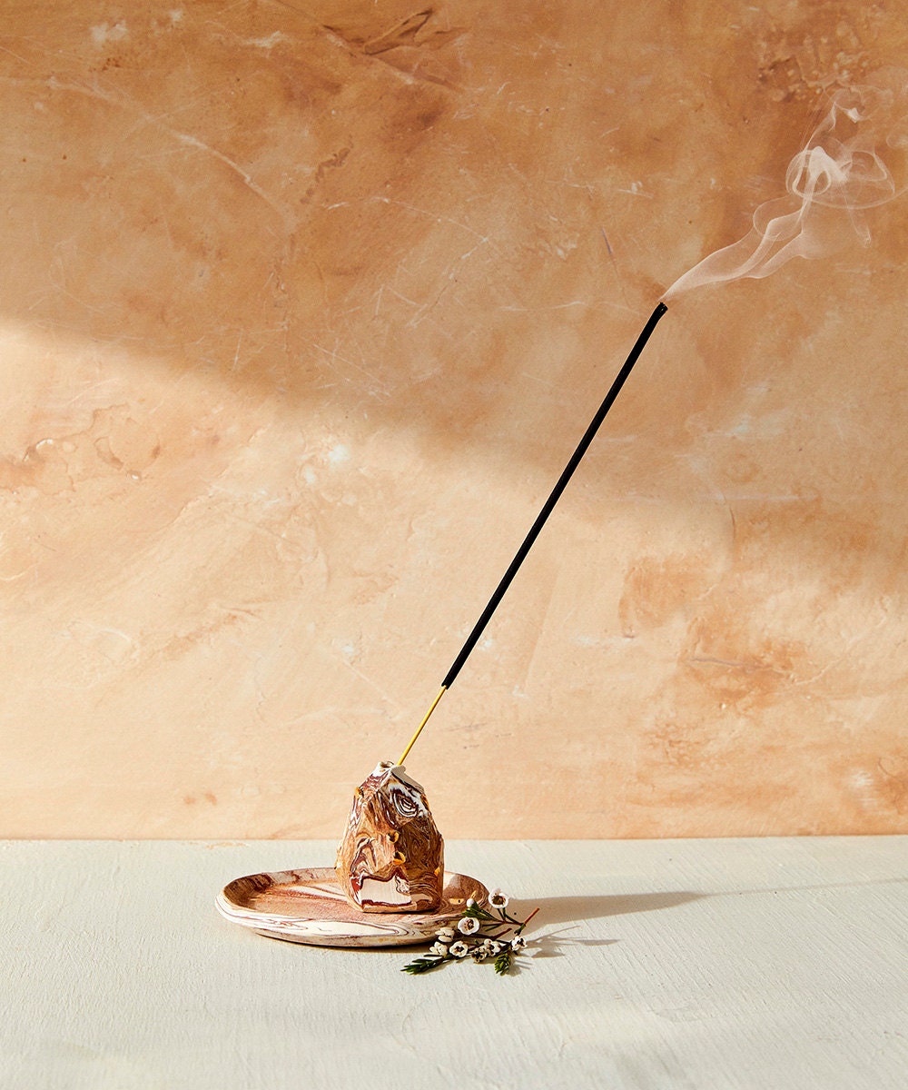 A stick of incense burns out of a marbled incense holder.
