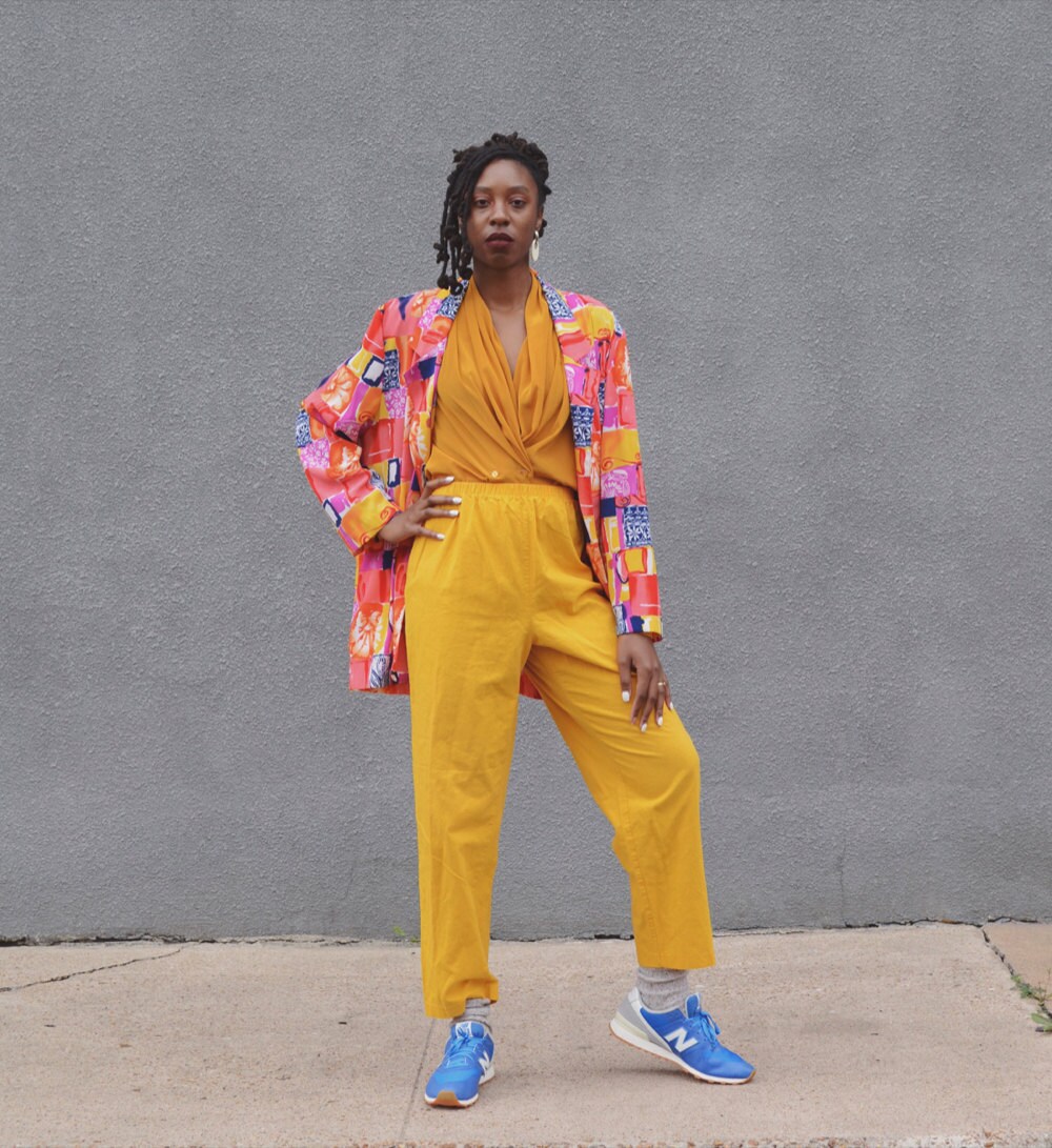 Rachelle models a colorful vintage outfit (including matching yellow pants and top, and a neon-multicolored jacket).