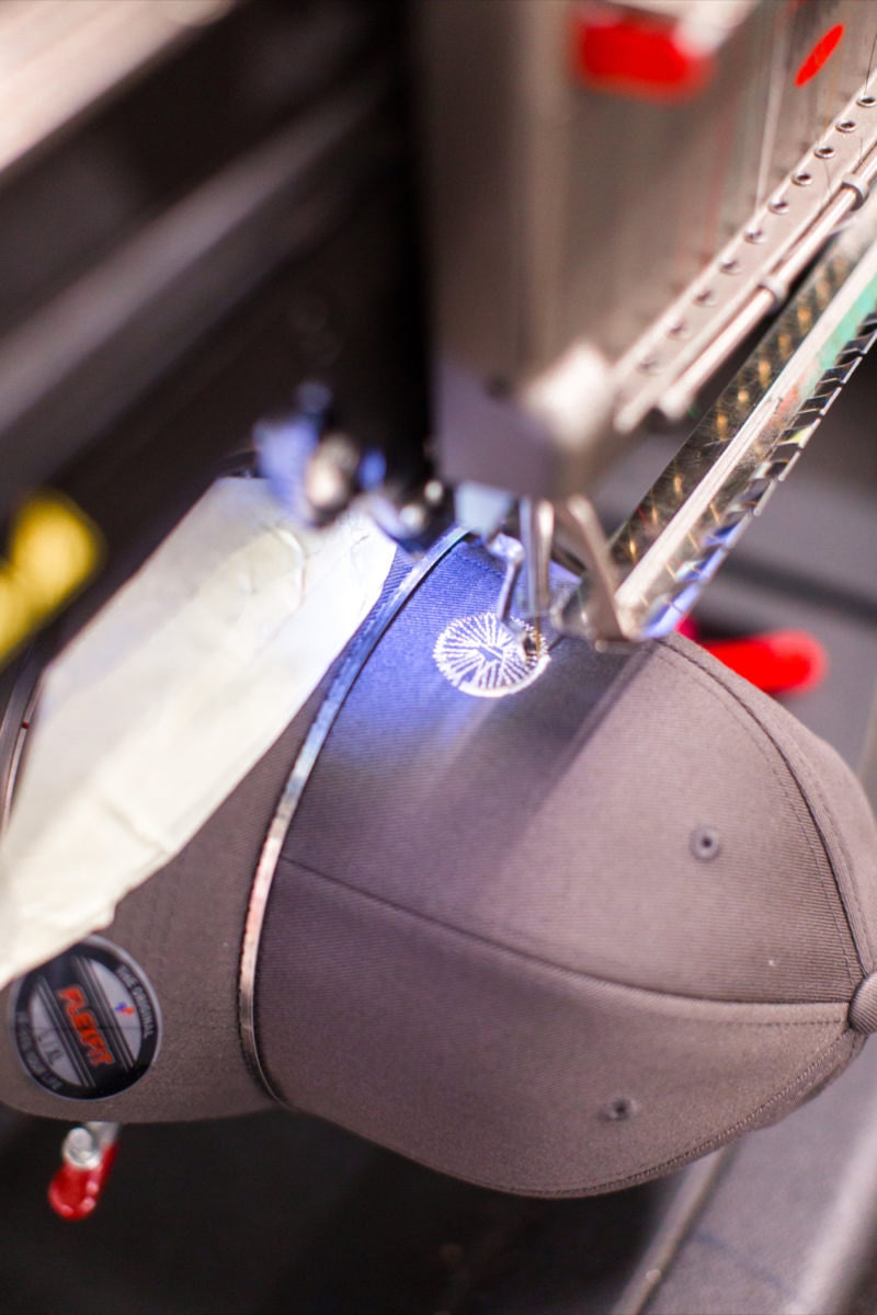 A machine embroidering a bicycle wheel onto a baseball cap.