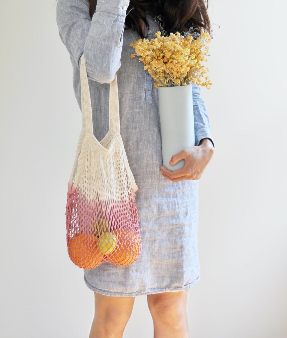 A woman carrying fresh produce in a pink dip-dyed netted market tote.