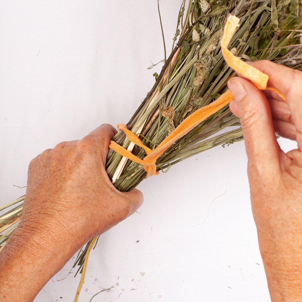 A person ties a ribbon around the stems of their newly assembled bouquet