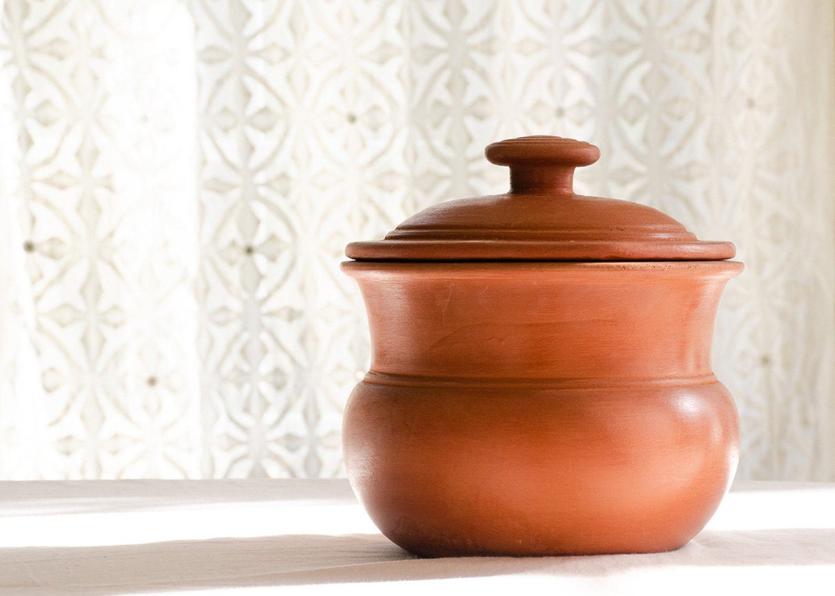 A terracotta curry pot with a white patterned curtain in the background