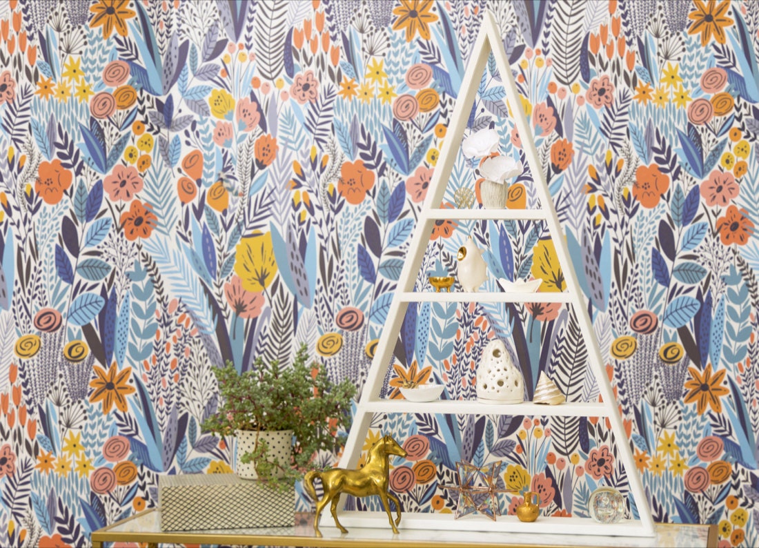 A shelf styled with white ceramics and gold-toned accents, displayed in front of colorful floral wallpaper.