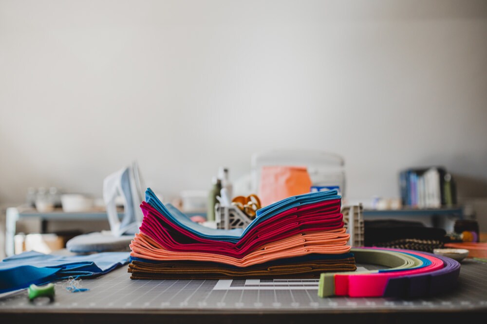 Colorful stacks of waxed canvas bags on a sewing table ready to be assembled.