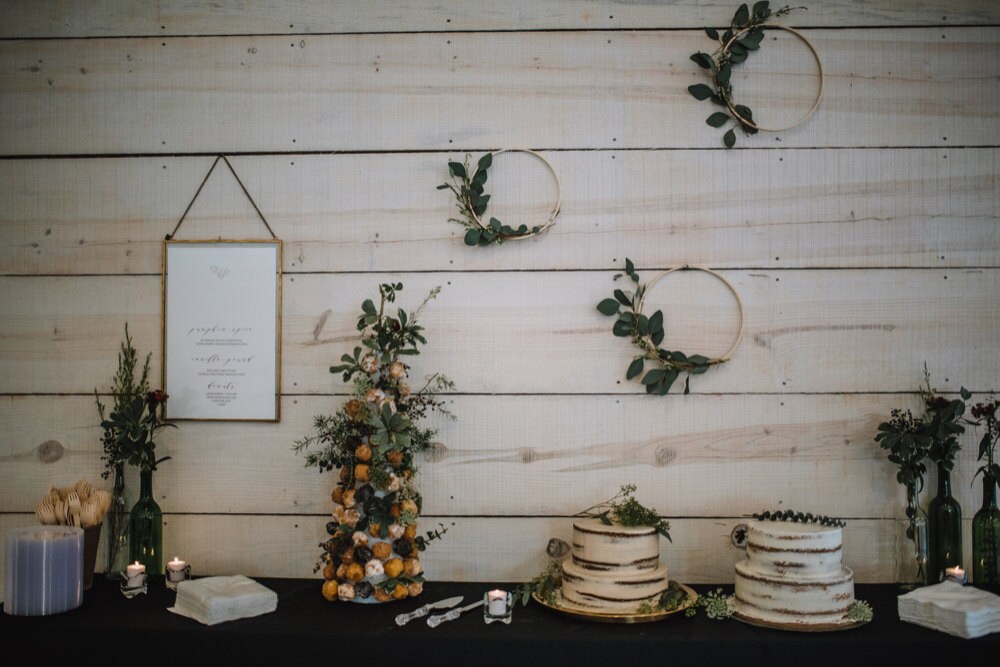 The dessert table, set with cakes and a donut stand, is accented by a trio of eucalyptus hoop wreaths on the wall behind it
