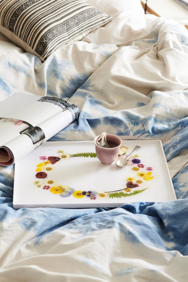 A styled photo of the completed DIY pressed flower tray laid out on a bed, carrying a cup of tea