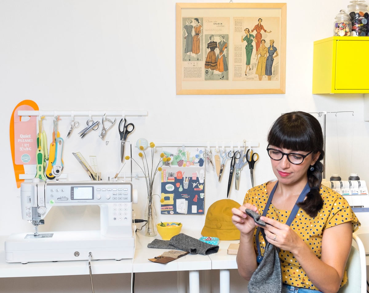 Simona sits at her desk and hand-stitches a piece