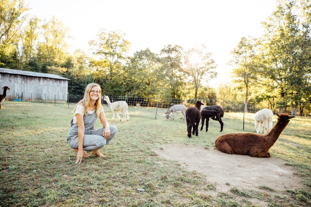 Kacie on the farm with several alpacas