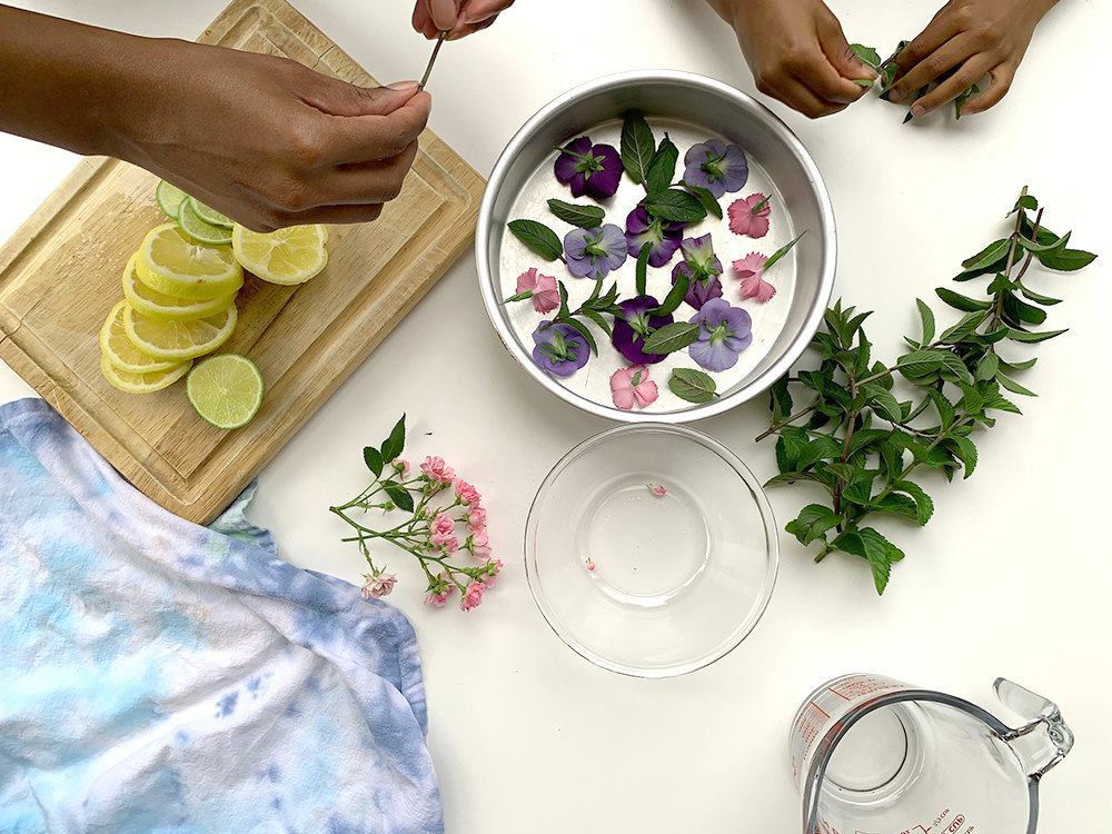 Aravis and her niece arrange flowers and mint leaves in the bottom of a cake pan.