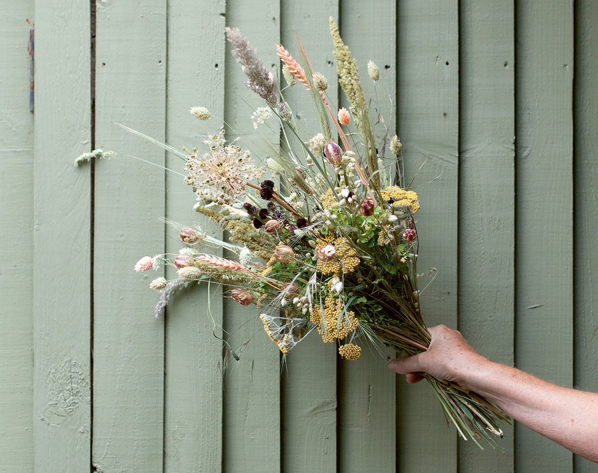 A bouquet of dried flowers held against a green wall.