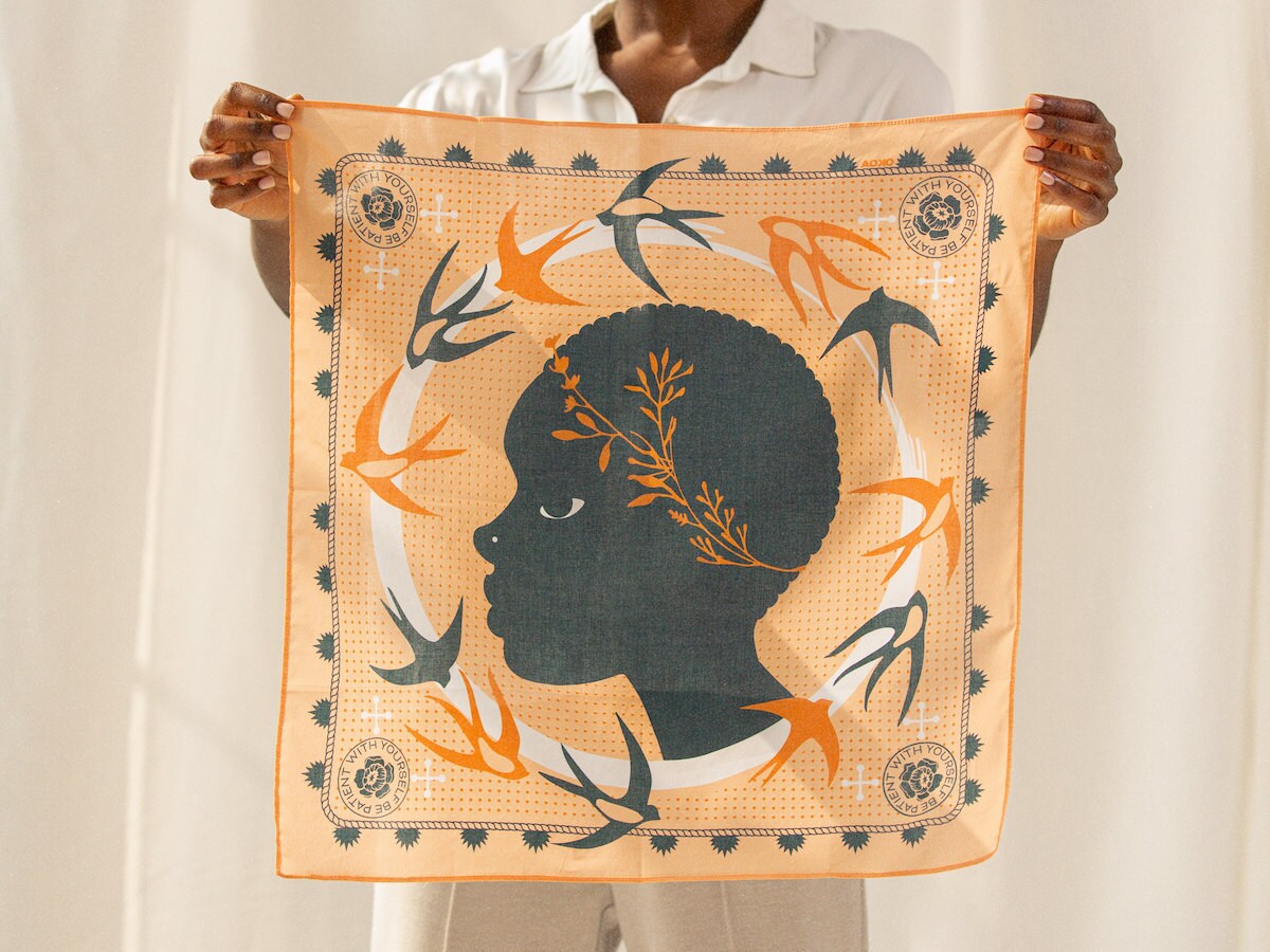 A woman holds up an elegant hand-illustrated scarf from All Very Goods