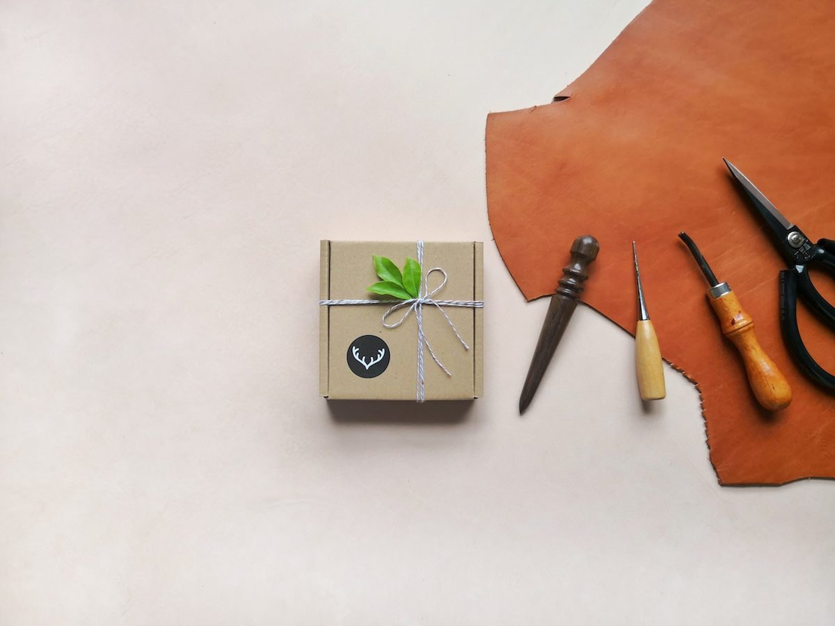 A packaged order displayed next to a piece of leather and four leatherworking tools