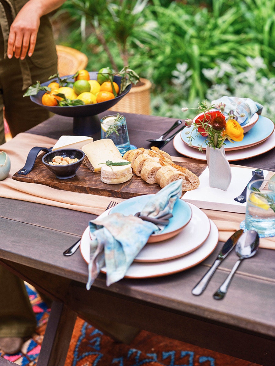 A large cutting board with bread and cheese sits on a decorated outdoor table