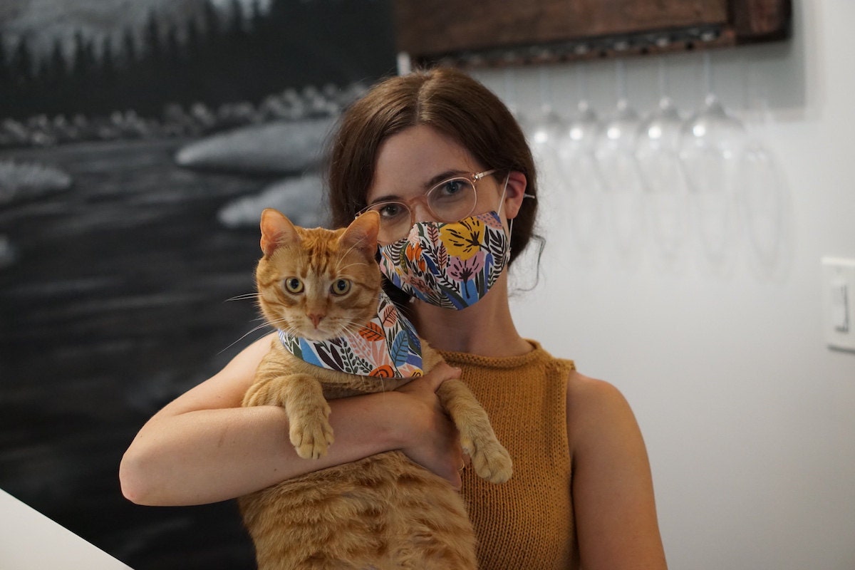 A woman and her cat wear a matching fabric face mask and bandana set.