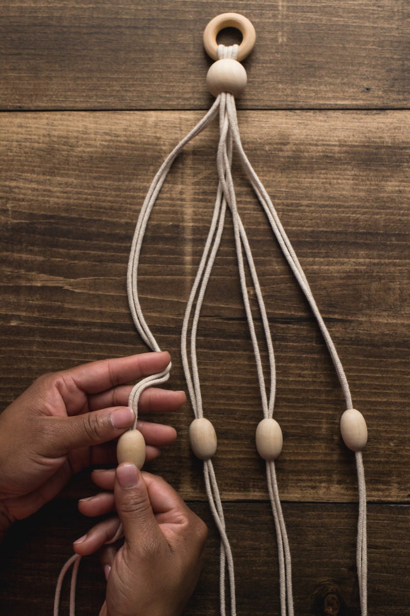 Hands separate the eight ropes into four groups of two and add a bead to each.