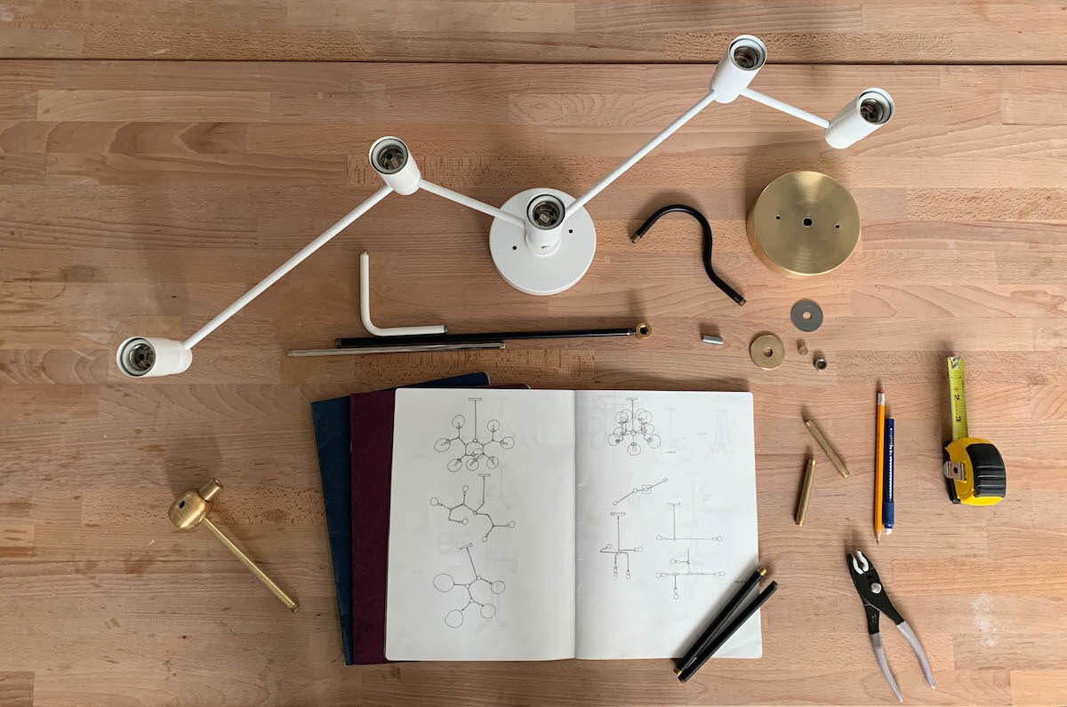 An open sketchbook containing illustrations of various lights sits on a table surrounded by light parts awaiting assembly