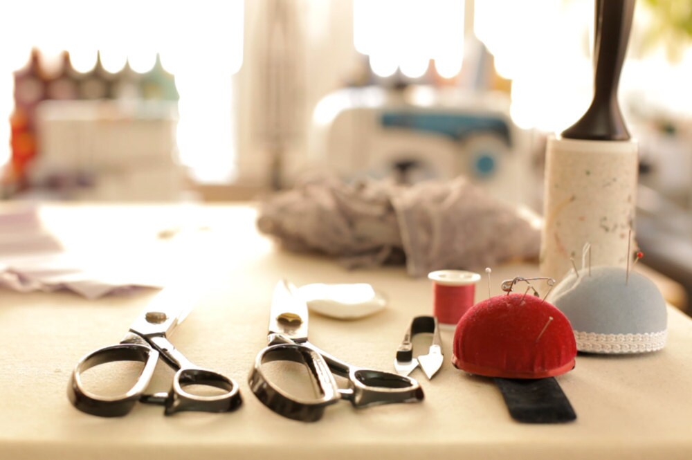 Scissors, pin cushions, thread, and other sewing materials lined up on Elma's workbench