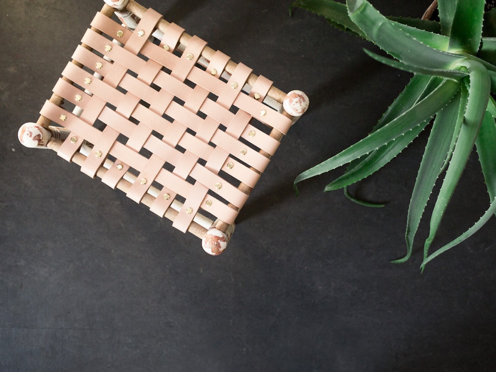 Finished stool with woven leather straps attached at all four edges